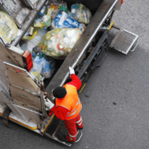 A man loading trash bags into the back of a garbage truck on a city street.